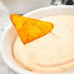 Chip in a bowl of 2 ingredient taco dip with more chips in the background.