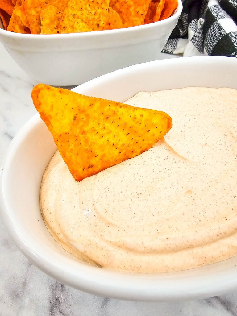Chip in a bowl of 2 ingredient taco dip with more chips in the background.