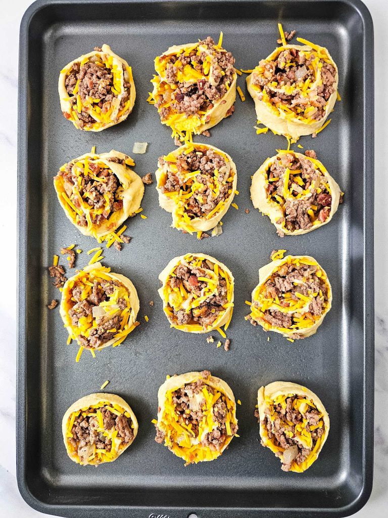 Bacon cheeseburger pinwheels on a baking sheet.