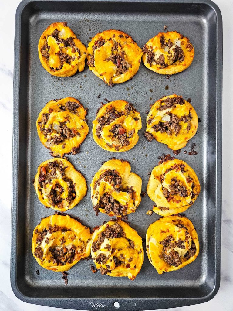 Baked bacon cheeseburger pinwheels in a baking sheet.