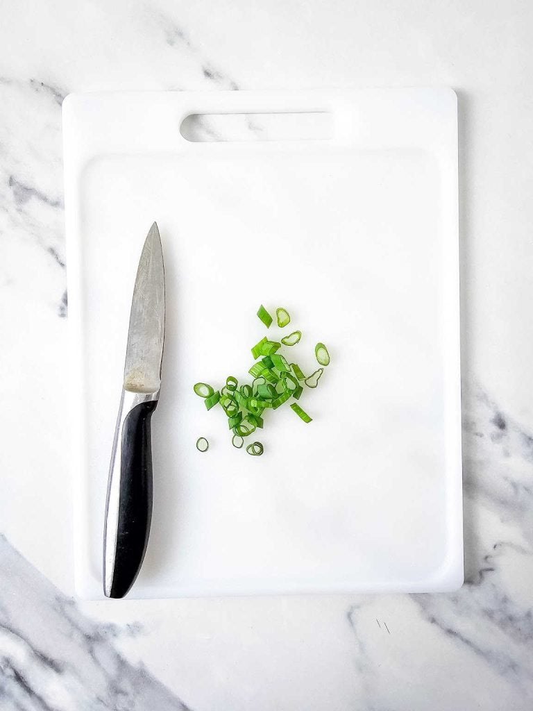 Chopped green onion and knife on a white cutting board.