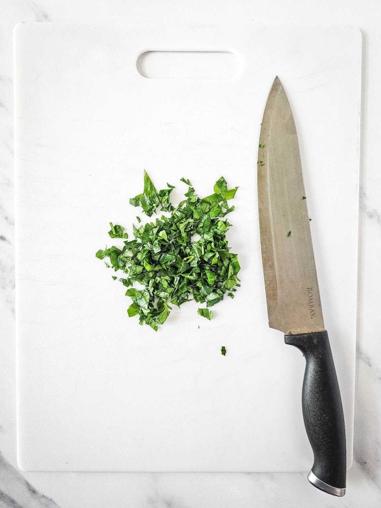 Chopped parsley and knife on a white cutting board.
