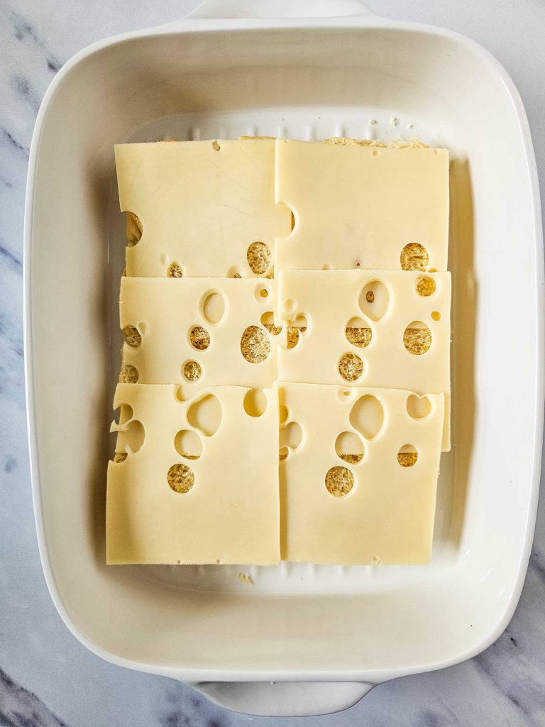 Slices of Swiss cheese spread over slider rolls in a casserole.