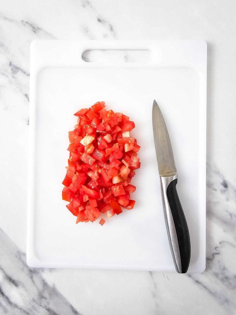 Diced tomatoes and knife on a white cutting board.