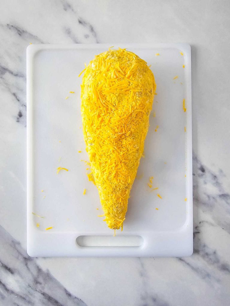 Carrot shaped cheeseball covered in shredded cheddar cheese.
