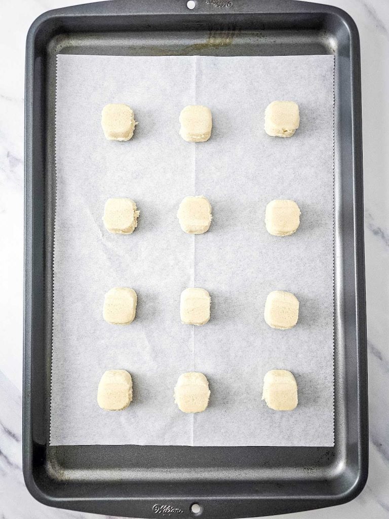 12 pieces of sugar cookie dough on a baking sheet.