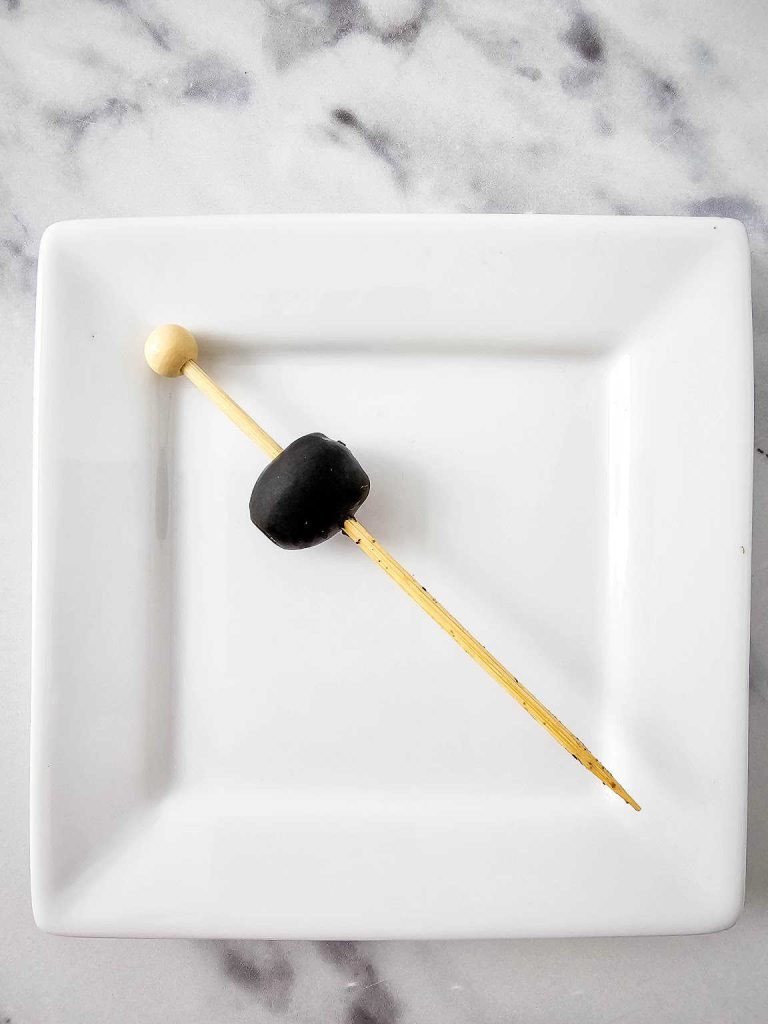 Skewered olive on a white plate.