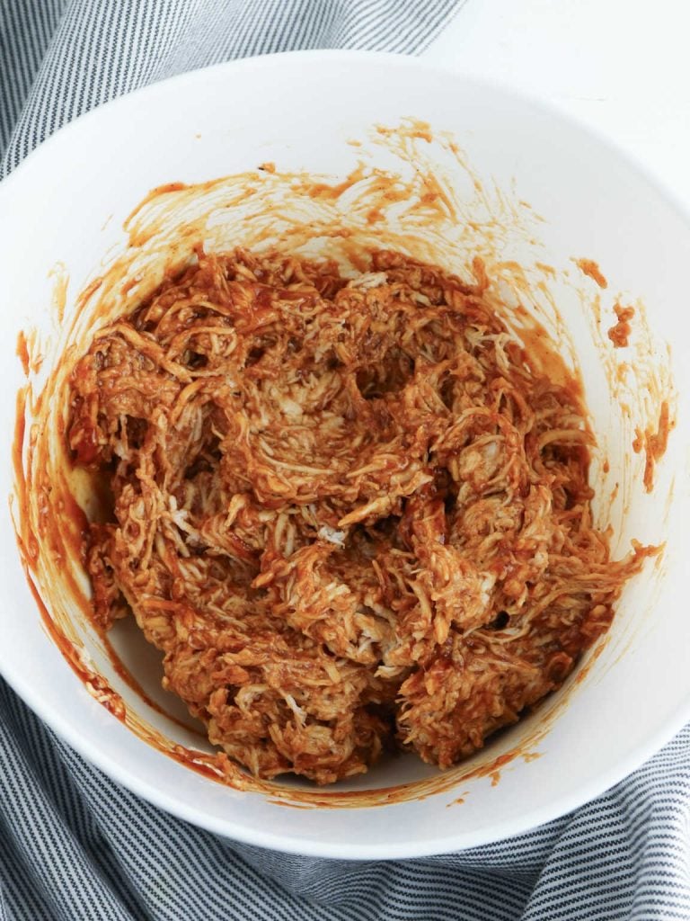 Mixture of shredded chicken and BBQ sauce in a large bowl.