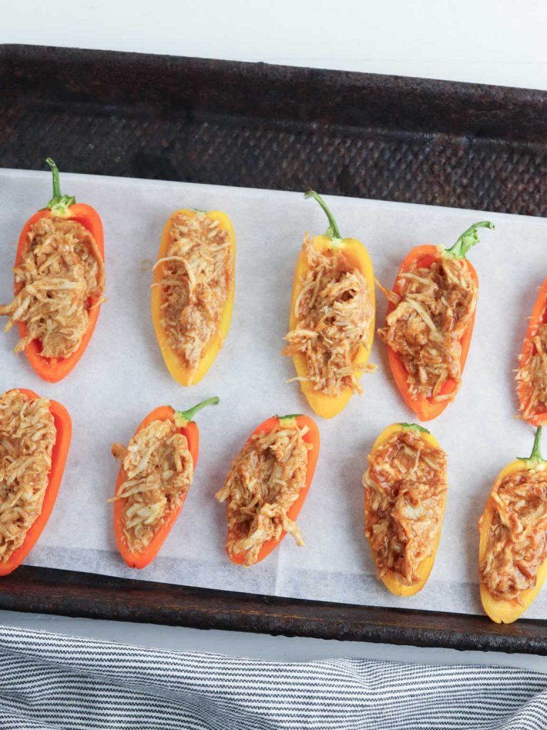 Mini peppers stuffed with shredded chicken mixture on a parchment paper lined baking sheet.