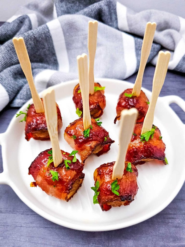 Bacon wrapped meatballs stuck with toothpicks on a white platter.