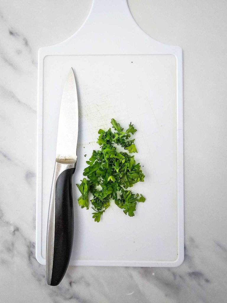 Chopped parsley and knife on a white cutting board.